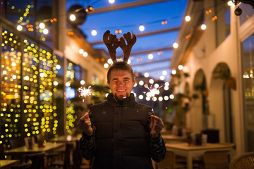 People, holidays and Christmas concept - young funny man in christmas deer costume with bengals light outdoors