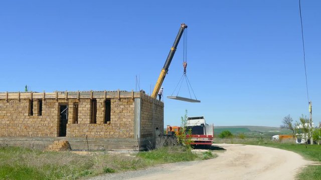The mobile crane drags the concrete slab to the unfinished house