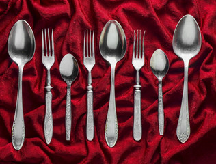 Vintage forks and spoons on a red silk tablecloth. Top view.