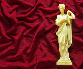 Antique souvenir statue of the Greek goddess on a red silk background. Copy space.