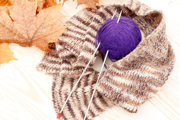 a ball of wool and around a scarf. two knitting needles stuck in them on a wooden background. There are yellow maple leaves without attention