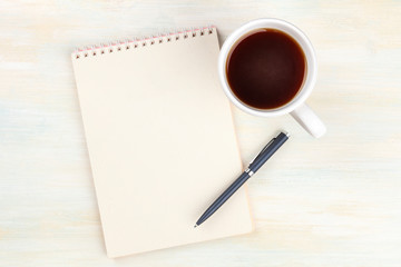 A photo of a blank page of a spiral notepad, with a cup of coffee, shot from the top on a wooden background with copy space