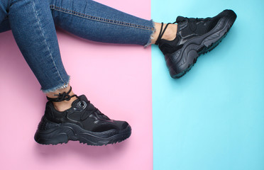 Women's legs in skin-tight jeans and trendy black dresses on a pastel background. Top view..