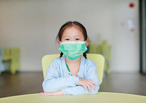Asian child girl wearing a protective mask sitting on kid chair in children room.