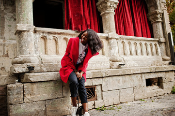 Stylish african american woman in red coat posed against old columns.