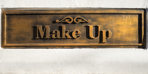 Gold embossed lettering Make Up on white wall.