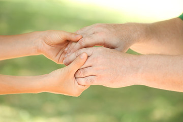 Helping hands on blurred background, closeup. Elderly care concept