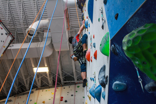 Young man wearing colorful sport clothing climbing on an advanced climbing wall indoors - lateral angle - Pictures taken in a climbing center in Quebec, Canada.