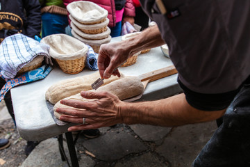 Man is scoring the bread by sliting it with a razor blade before putting it into an outdoor bread oven - Pictures taken during a bread and pizza making workshop