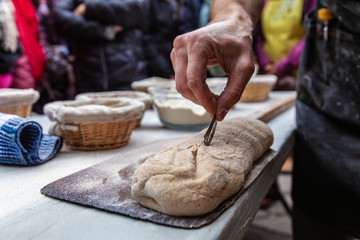Man is scoring the bread by sliting it with a razor blade before putting it into an outdoor bread oven - close up - Pictures taken during a bread and pizza making workshop