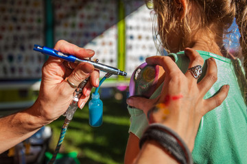 Young girl getting an airbrush stencil temporary tattoo in a family festival outdoors - Closeup...