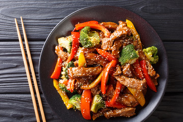 Stir-fried teriyaki beef with red and yellow bell pepper, broccoli and sesame seeds close-up on the...