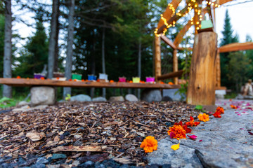 Wooden structure with various colors of silk lantern boats displayed and flower petals scattered on the floor all around - 2/2 - Wide angle picture taken outside in northern Quebec, Canada