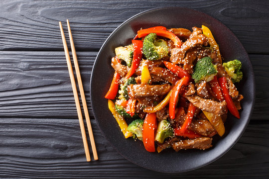 delicious Asian teriyaki beef with red and yellow bell peppers, broccoli and sesame seeds close-up on a plate. horizontal top view