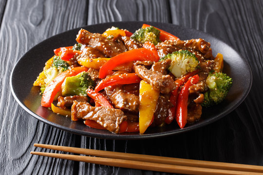 Asian food: teriyaki beef with red and yellow bell peppers, broccoli and sesame seeds close-up on a plate. horizontal