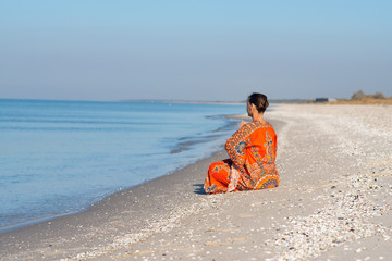 Fototapeta na wymiar Woman in ethnic dress relaxes and meditates on a deserted beach