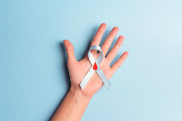 Helping hand holding blue ribbon awareness with red blood drop on a blue background.
