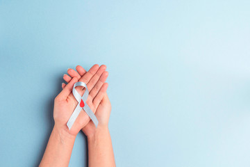Helping hands holding blue ribbon awareness with red blood drop on a blue background. World...