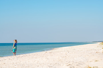 Fototapeta na wymiar Woman in a pareo walks along the sandy deserted beach