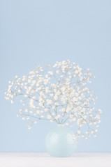 Spring branch with small white flowers in blue sphere vase in soft light blue modern interior, on a white table.