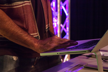 DJ wearing rough cotton sleeveless jacket is scrolling though his music on his professionnal laptop while mixing live