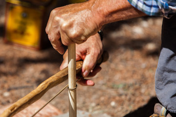 Native man is lighting a campfire using the hand drill technique and primitive tools as part of a...