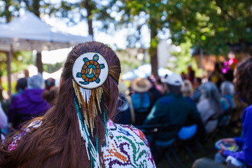 Woman is wearing a large turtle beaded hair pin and colorful native clothing while listening to a...