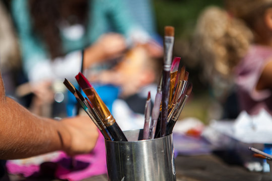 Metal container full of paintbrushes while kids are sitting outside during an artistic workshop - Pictured at an artistic workshop in a family festival
