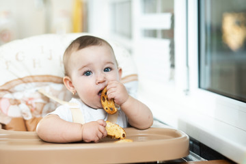 Baby girl eating cracker with raisins in a chair