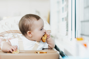 Baby girl eating cracker with raisins in a chair