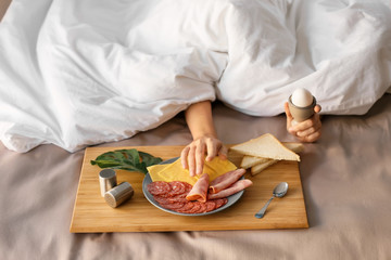 Sleepy woman under blanket with delicious breakfast on bed