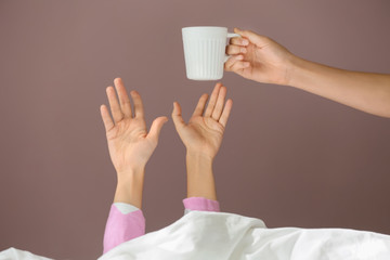 Giving of hot coffee to sleepy woman under blanket in bed