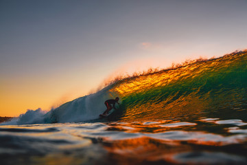 Surfer ride on barrel wave at warm sunset. Professional surfing in ocean, Bingin beach