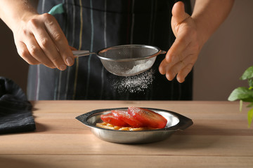 Woman sprinkling sweet pear stewed in wine with sugar powder, closeup