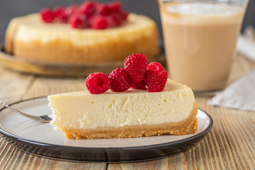 Piece of classic cheesecake with raspberries and coffee on a wooden background. Copy space.