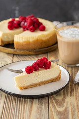 Piece of classic cheesecake with raspberries and coffee on a wooden background. Copy space.