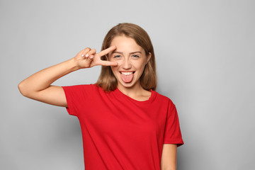 Fototapeta premium Portrait of funny young woman showing victory gesture on light background