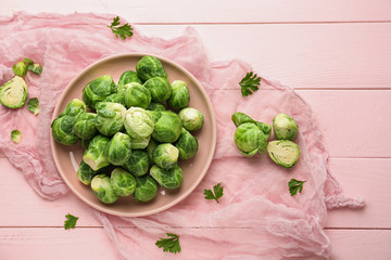 Plate with fresh brussels sprouts on color wooden table, top view