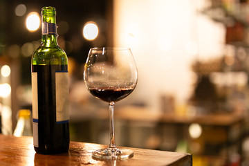 Shot in low light and high iso bottle and glass of red wine on wooden top.