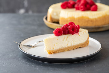 Slice of New York Cheesecake with raspberries on a dark background.