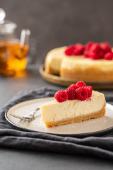 Slice of New York Cheesecake with raspberries on a dark background.