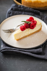 Slice of New York Cheesecake with raspberries on a dark background.