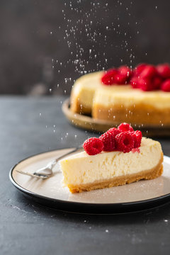 Slice of New York Cheesecake with raspberries on a dark background.