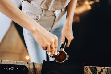 A young pretty slim girl,wearing casual outfit,is cooking coffee in a modern coffee shop. It focuses on the process.