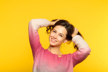 happy joyful smiling girl making pig tails from her hair. relaxed carefree teenage lifestyle and childish behavior. young beautiful brown haired woman portrait on yellow background.