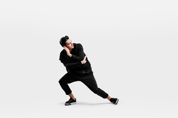 Handsome dancer dressed in a stylish black clothes is dancing street dance. He makes stylized movements with his hands