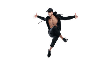 Young handsome young dancer dressed in black pants, a sweatshirt on a naked torso jumps and spreads his arms to the sides