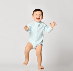 Infant child baby boy kid toddler in light blue body cloth make first steps on grey  