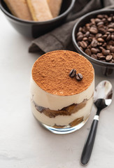 Traditional Italian dessert tiramisu in a glass on a white stone background. Copy space.