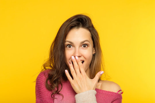surprised shocked astonished amazed girl covering mouth with hand. unbelievable news. young beautiful woman on yellow background. emotional reaction concept.